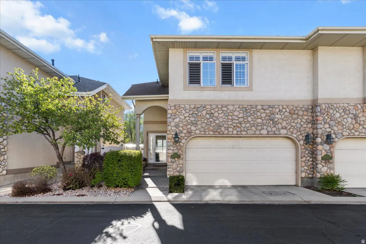 View of front facade featuring stone siding, stucco siding, an attached garage, and driveway