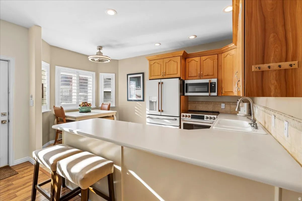 Kitchen with high end white fridge, range with electric stovetop, light countertops, stainless steel microwave, and a peninsula