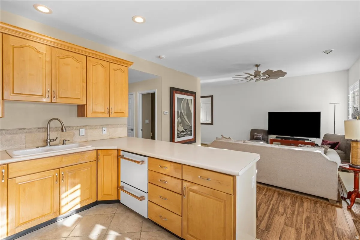 Kitchen featuring a peninsula, light countertops, open floor plan, a ceiling fan, and dishwasher