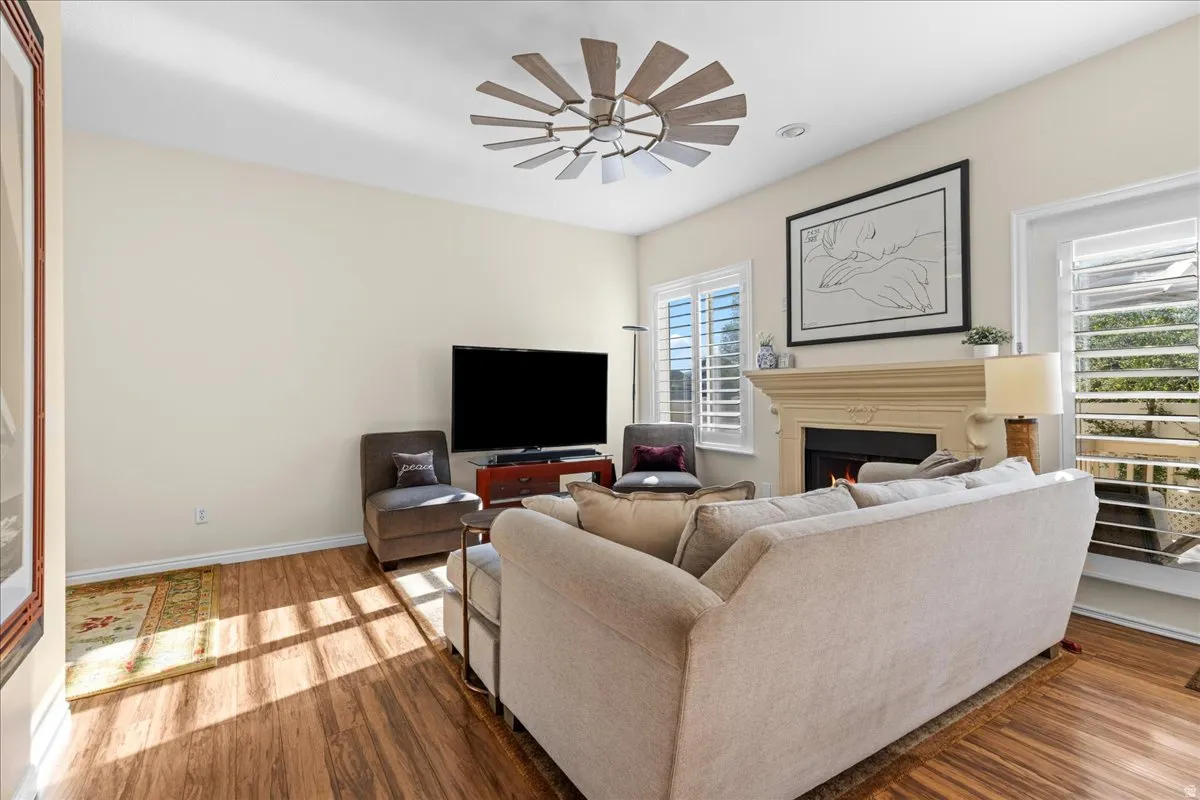 Living room featuring wood finished floors, ceiling fan, and a warm lit fireplace