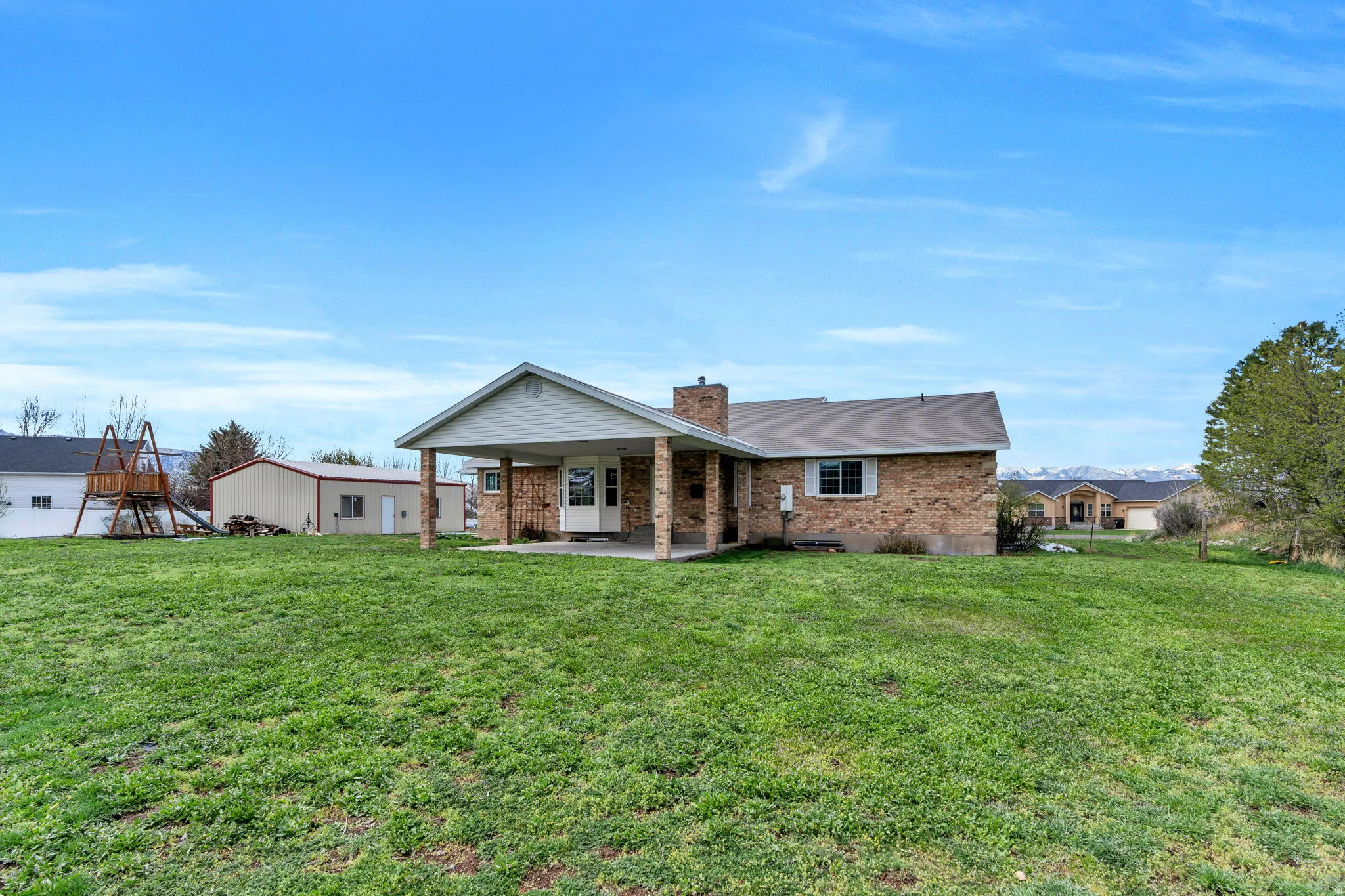View of front of property featuring a patio, brick siding, a chimney, and a front lawn