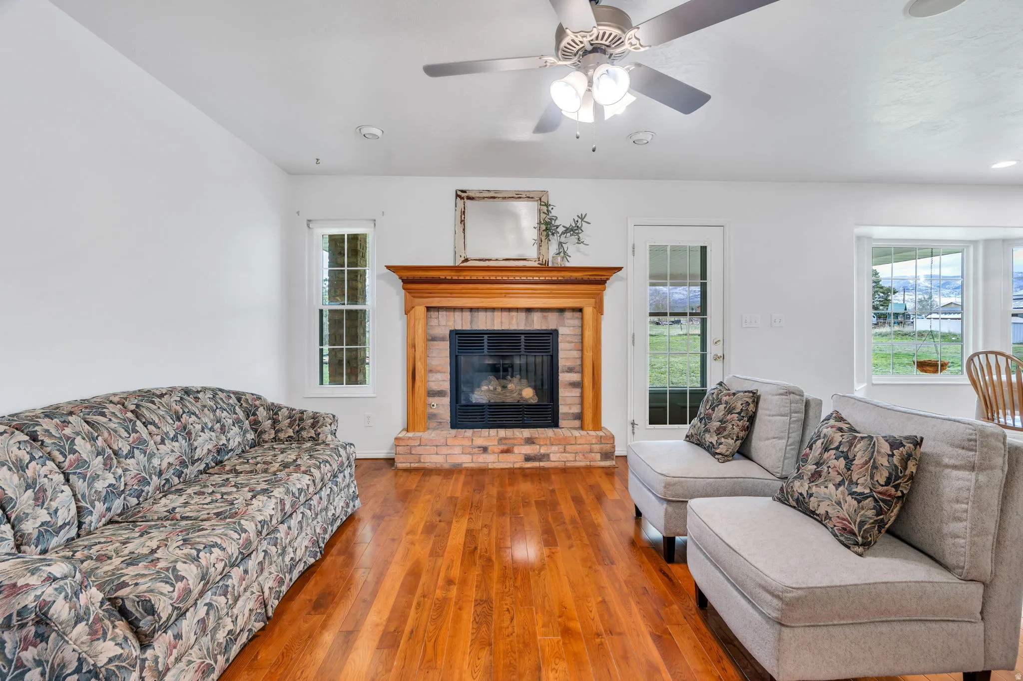 Living area featuring wood-type flooring, a ceiling fan, and a brick fireplace