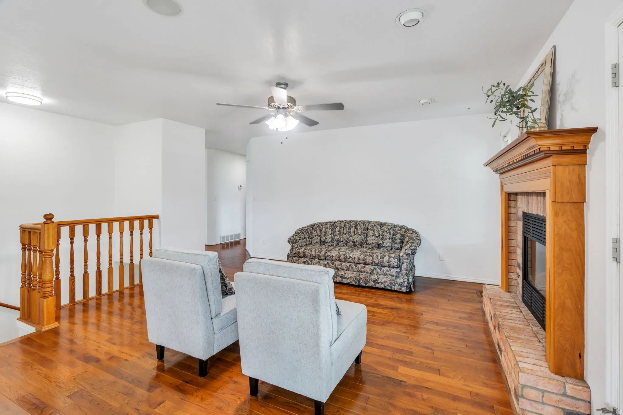Living area with hardwood / wood-style flooring, a fireplace, an upstairs landing, and ceiling fan
