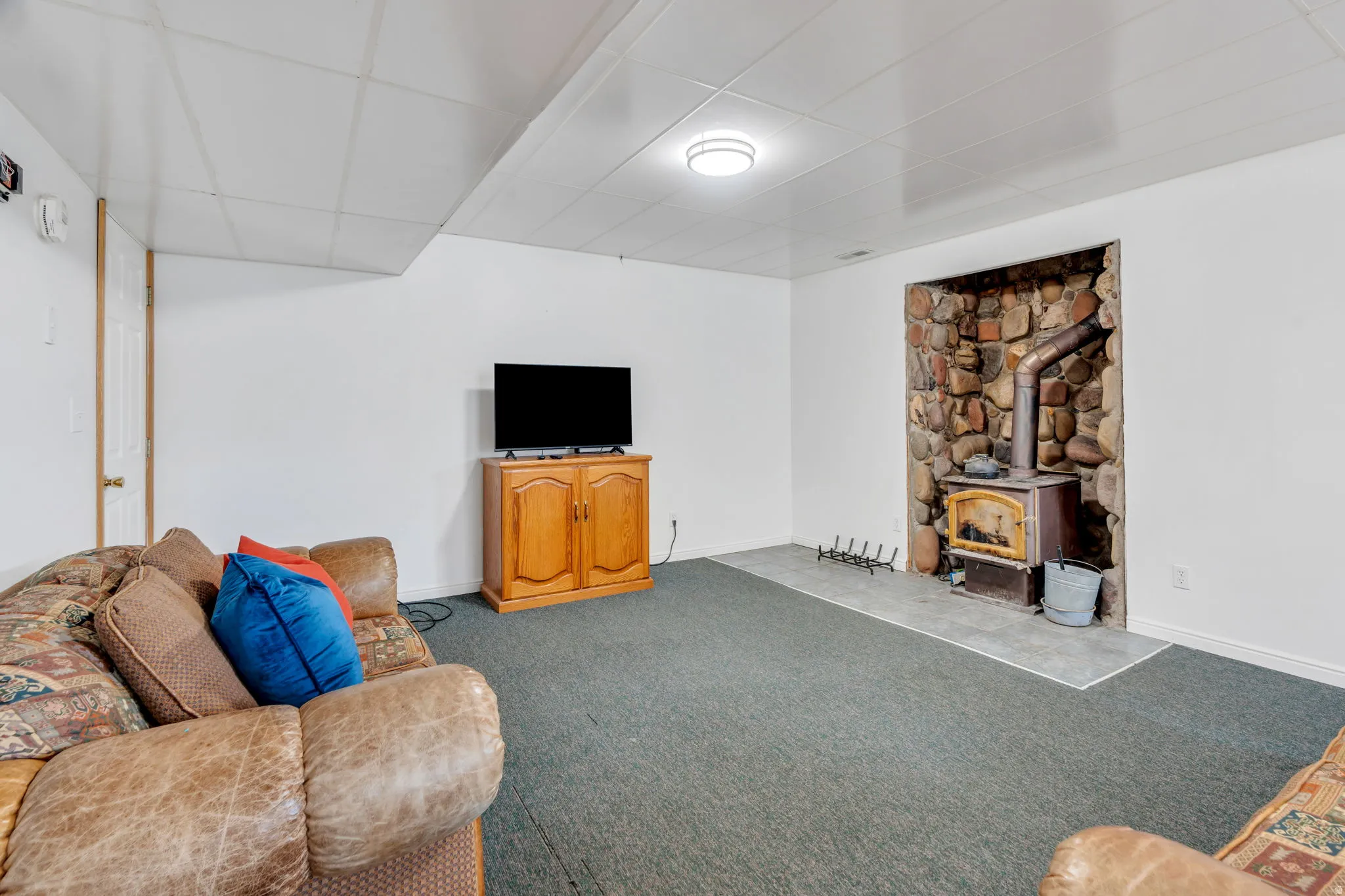 Living room with a wood stove, a paneled ceiling, and light carpet