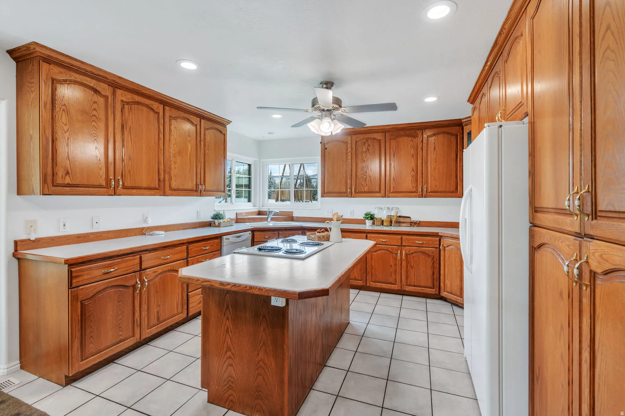 Kitchen with wood finish cabinetry, white appliances, ceiling fan, light countertops, and recessed lighting
