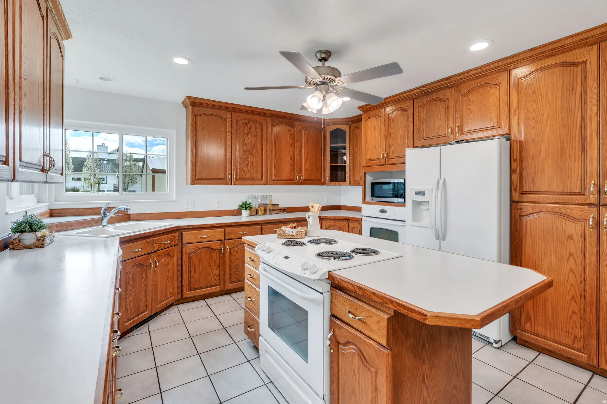 Kitchen featuring white appliances, light countertops, a center island, wood finish cabinetry, and glass insert cabinets