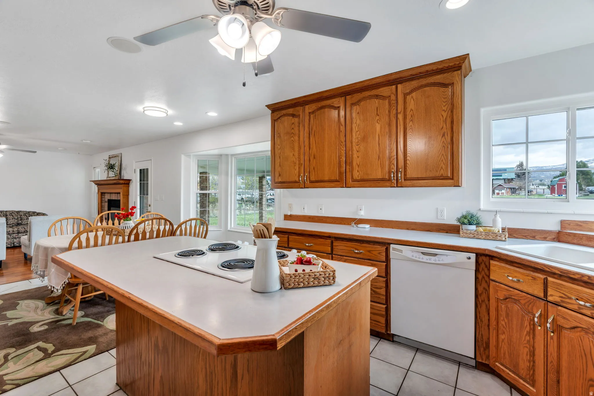 Kitchen with a ceiling fan, white appliances, wood finish cabinetry, a center island, and light countertops