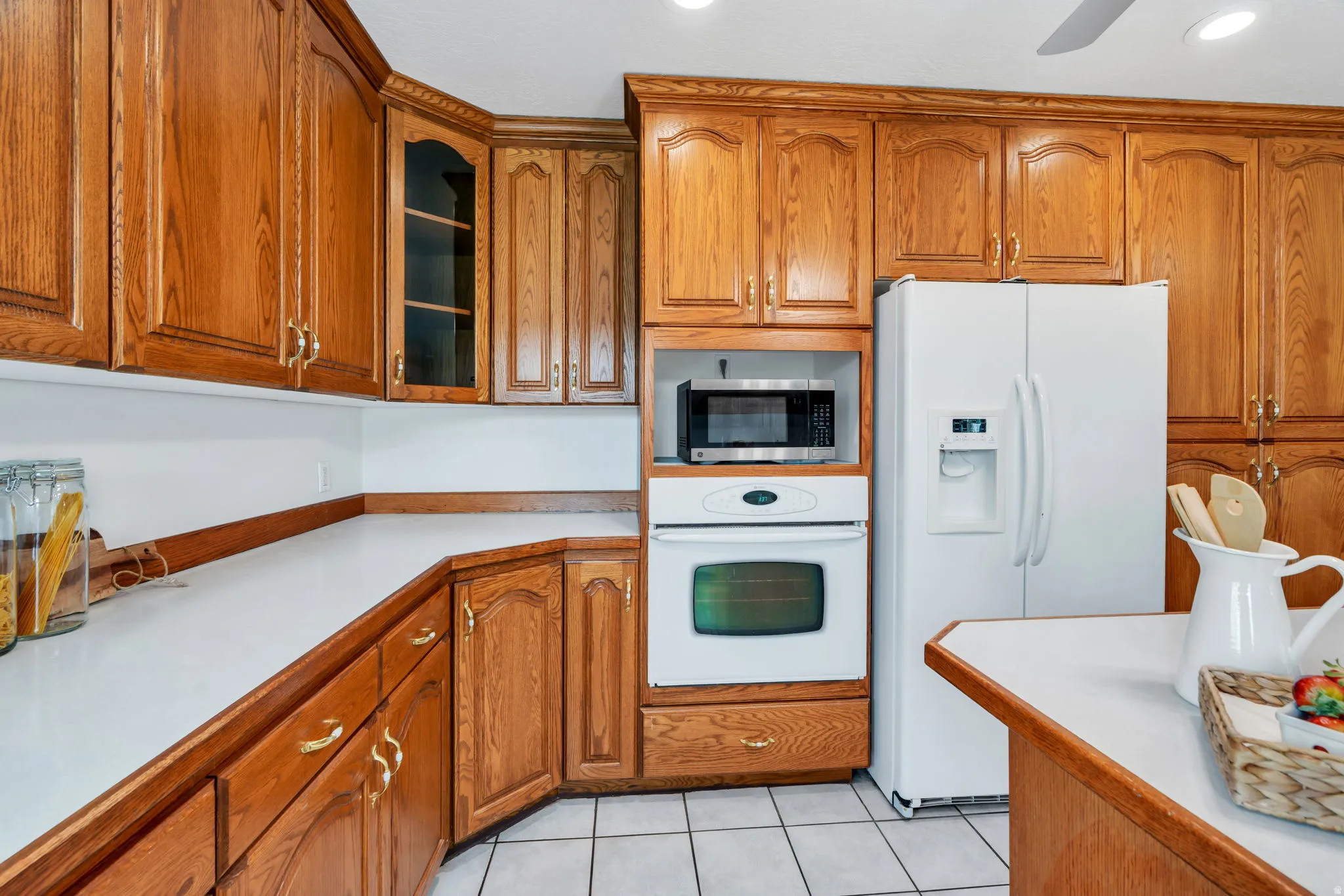 Kitchen featuring light countertops, white appliances, wood finish cabinets, glass fronted cabinets, and light tile patterned flooring