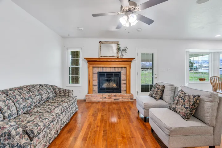 Living area featuring wood-type flooring, a ceiling fan, and a brick fireplace