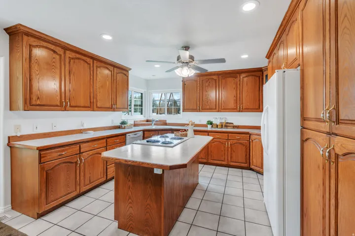 Kitchen with wood finish cabinetry, white appliances, ceiling fan, light countertops, and recessed lighting