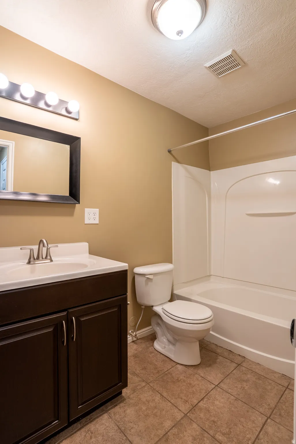 Bathroom featuring vanity, shower / bath combination, a textured ceiling, and light tile patterned floors