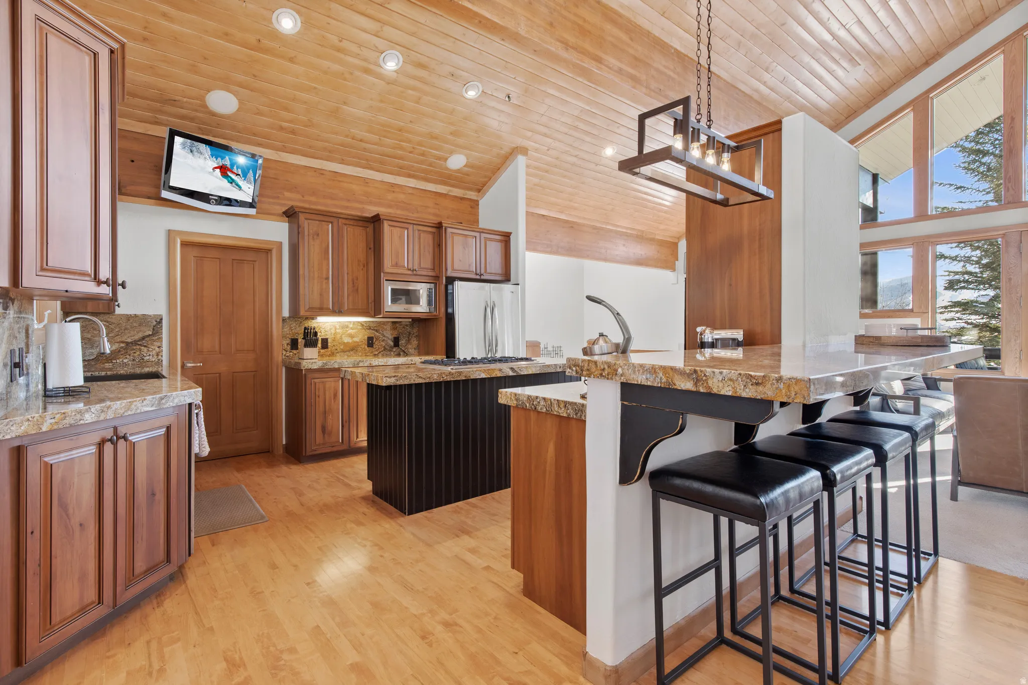 Kitchen featuring wood finish cabinetry, decorative light fixtures, light wood-style flooring, a high wood ceiling, and a breakfast bar area