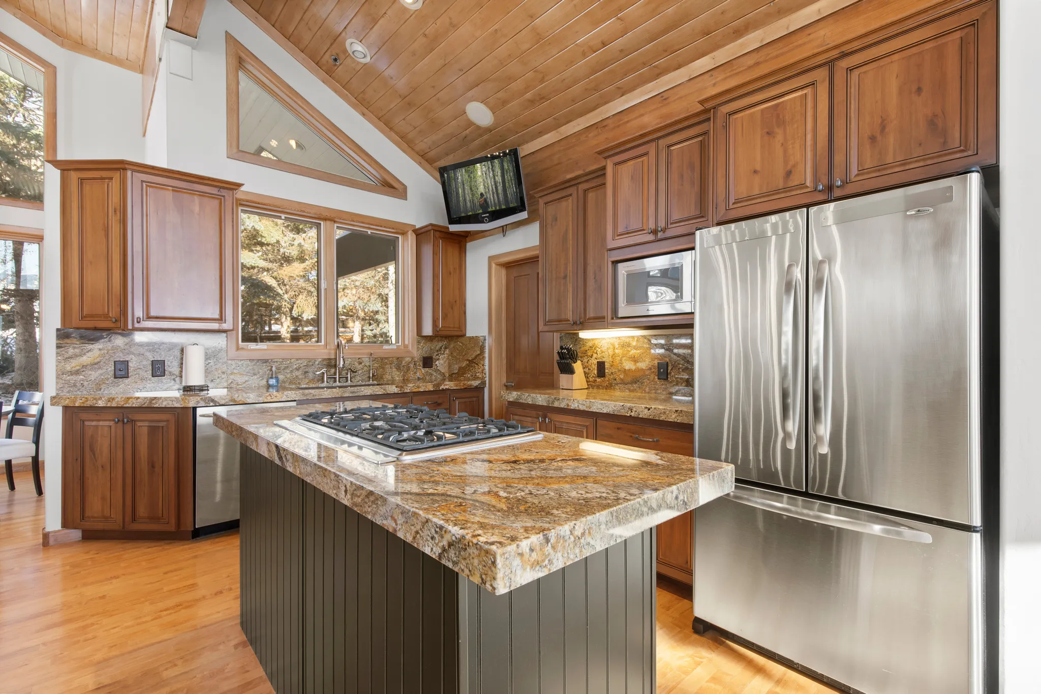 Kitchen featuring stainless steel appliances, decorative backsplash, a vaulted wooden ceiling, light wood-style flooring, and a kitchen island