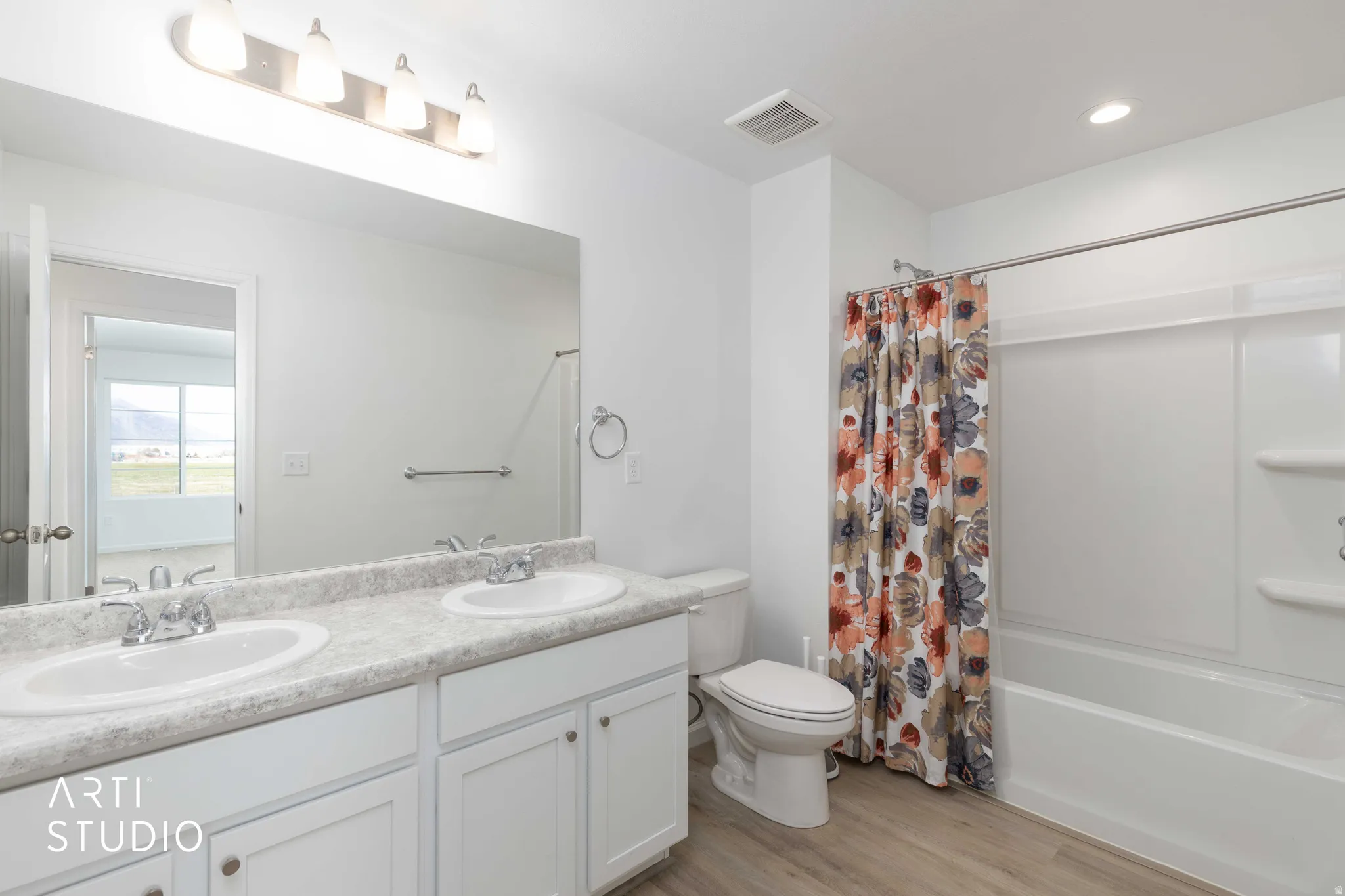 Bathroom featuring double vanity, light wood finished floors, shower / tub combo with curtain, and recessed lighting