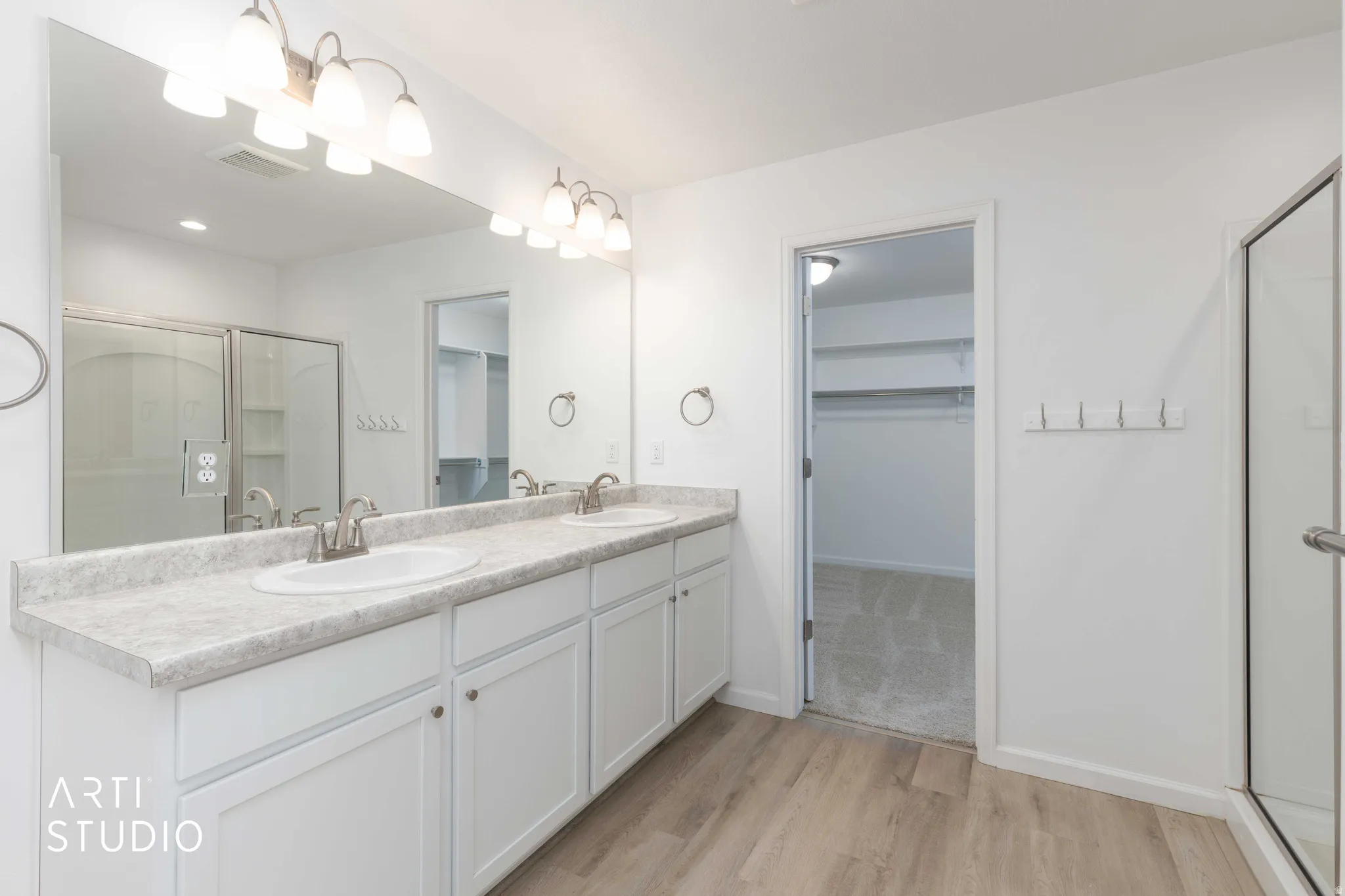 Bathroom featuring a spacious closet, a shower stall, double vanity, and light wood-style flooring