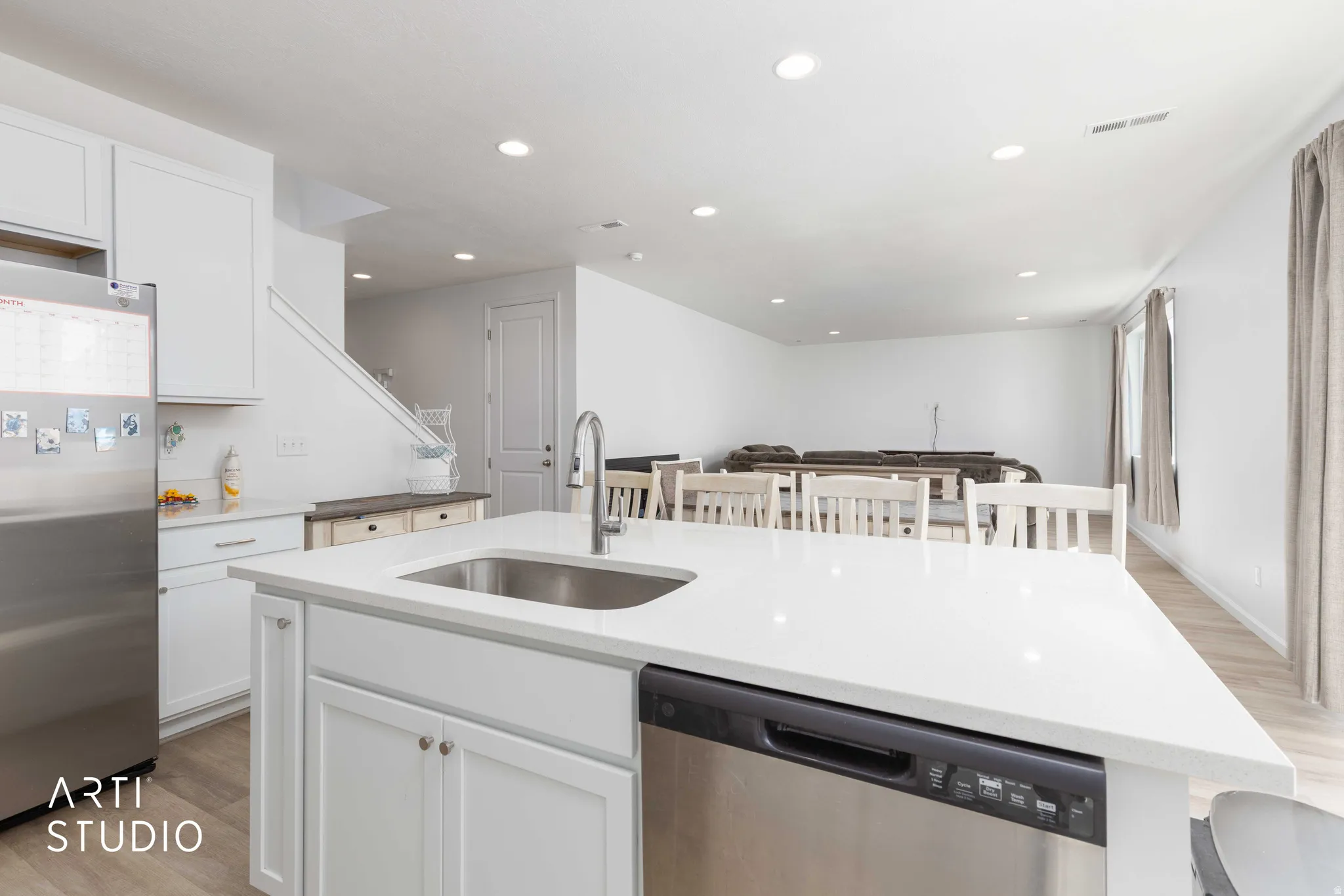 Kitchen featuring light wood finished floors, stainless steel appliances, white cabinetry, an island with sink, and light stone counters