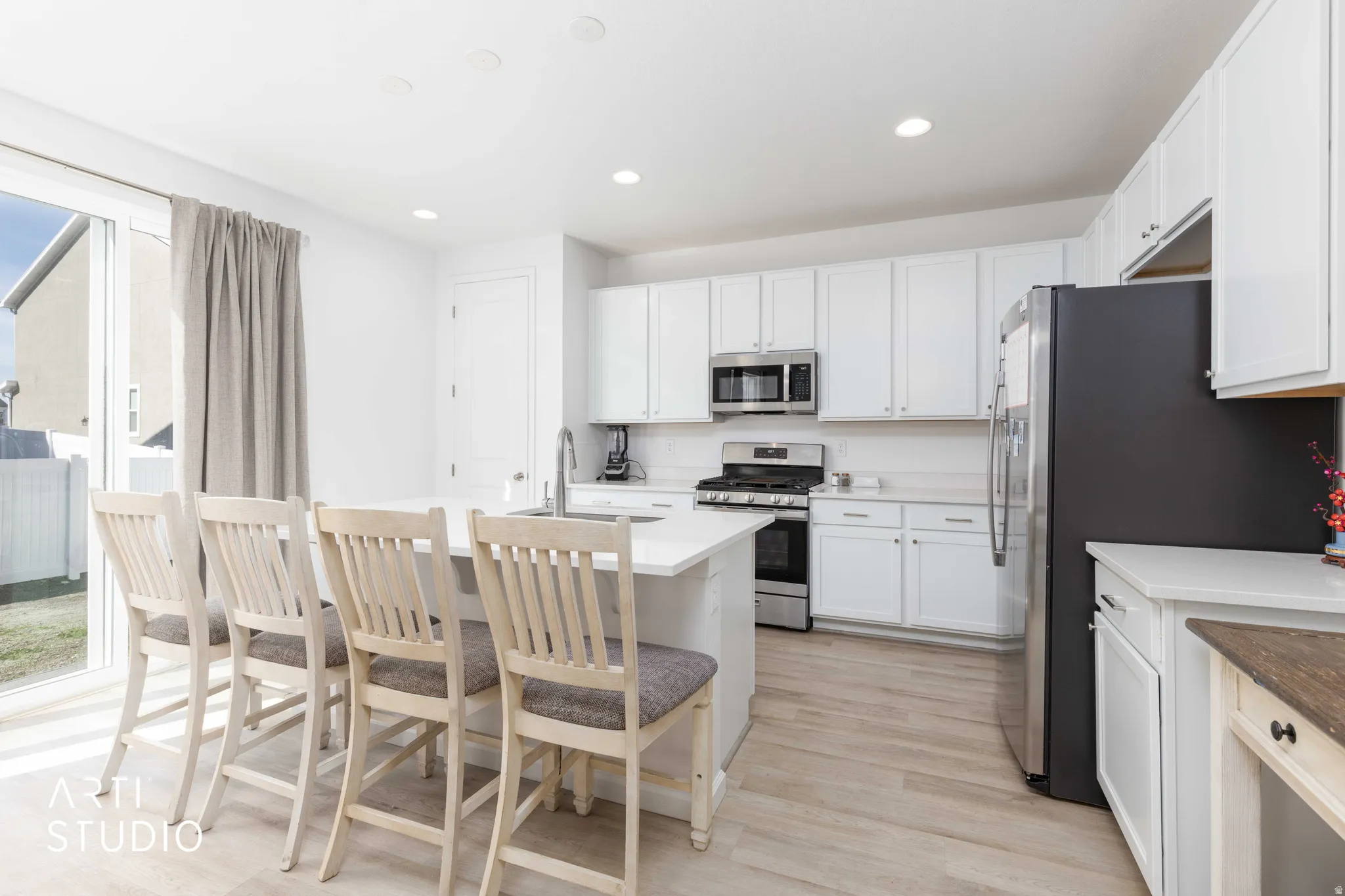 Kitchen with stainless steel appliances, recessed lighting, white cabinetry, light wood-type flooring, and an island with sink