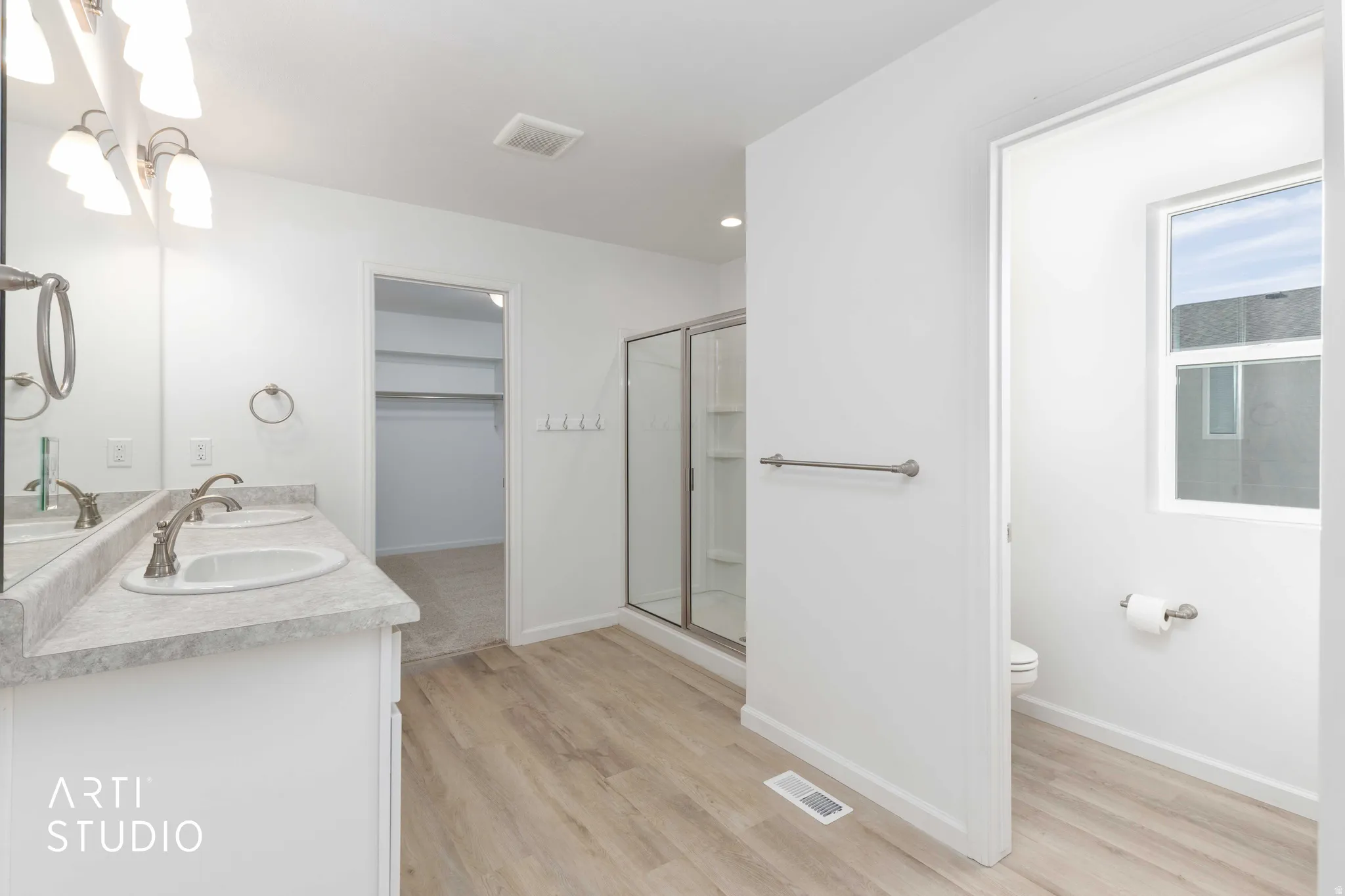 Bathroom featuring double vanity, a stall shower, light wood finished floors, a walk in closet, and recessed lighting