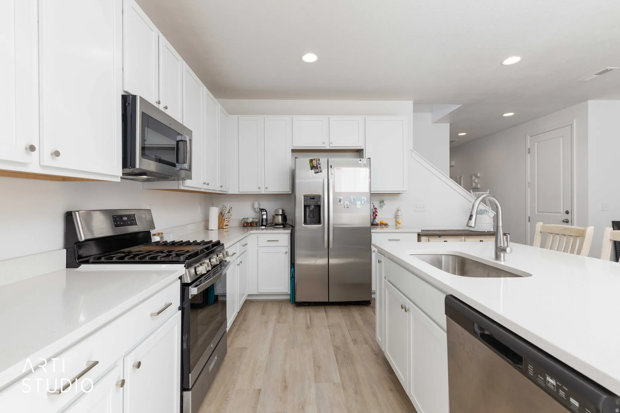 Kitchen with stainless steel appliances, white cabinetry, light wood-type flooring, recessed lighting, and light stone counters