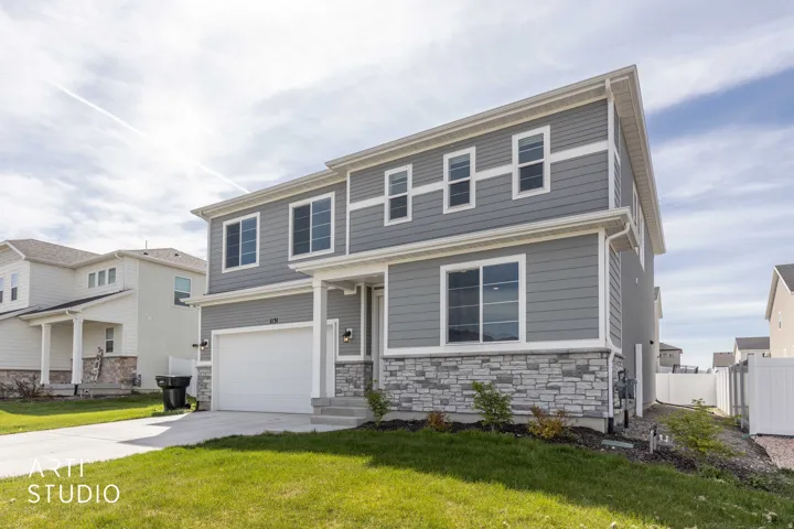 View of front facade featuring a garage, stone siding, and driveway