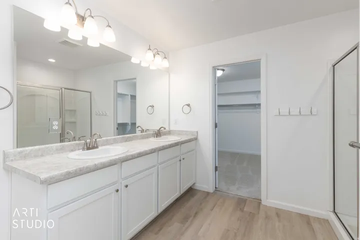 Bathroom featuring a spacious closet, a shower stall, double vanity, and light wood-style flooring