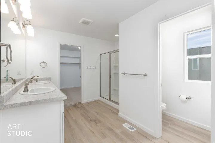 Bathroom featuring double vanity, a stall shower, light wood finished floors, a walk in closet, and recessed lighting