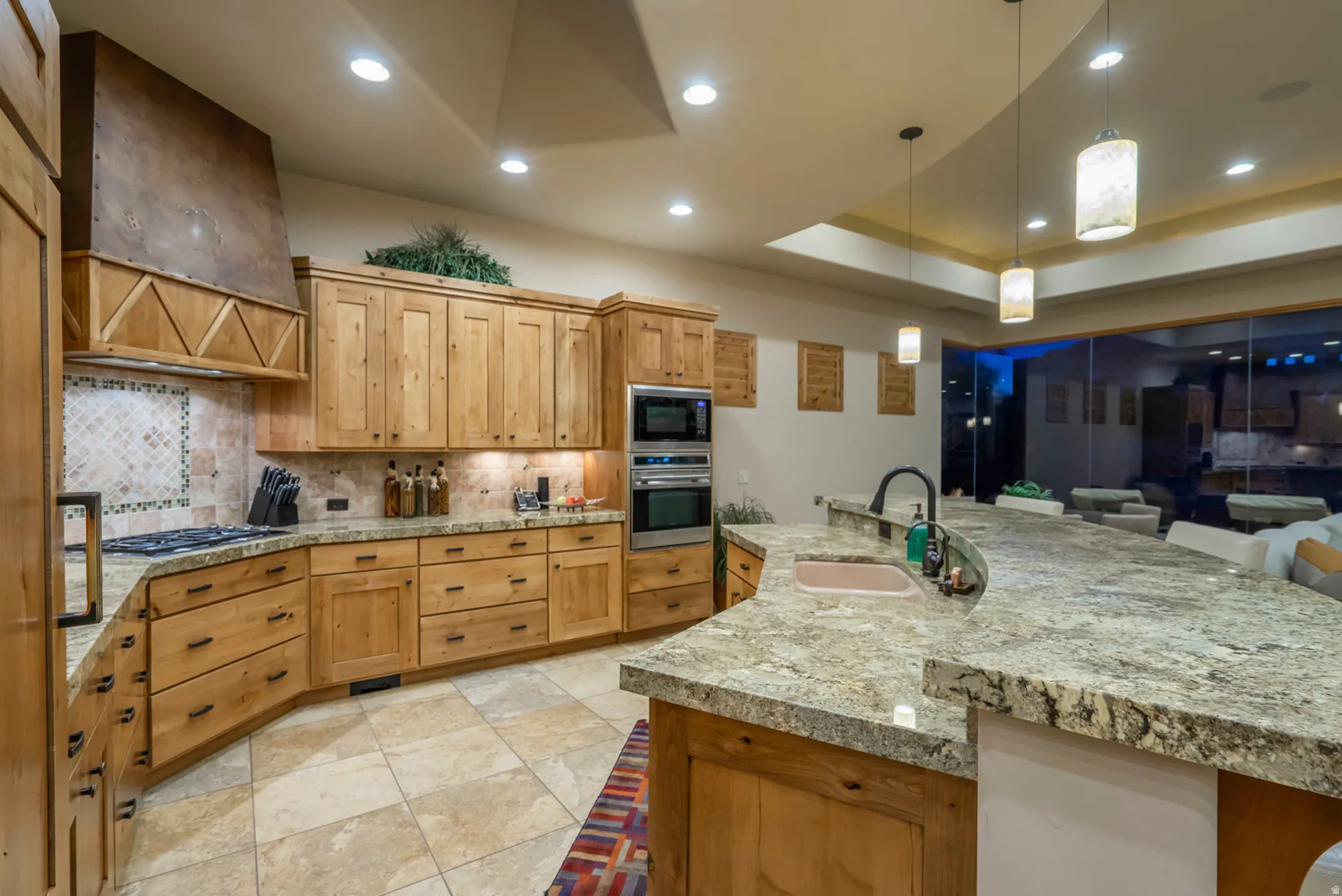 Kitchen with a raised ceiling, stainless steel appliances, light stone countertops, decorative light fixtures, and a breakfast bar