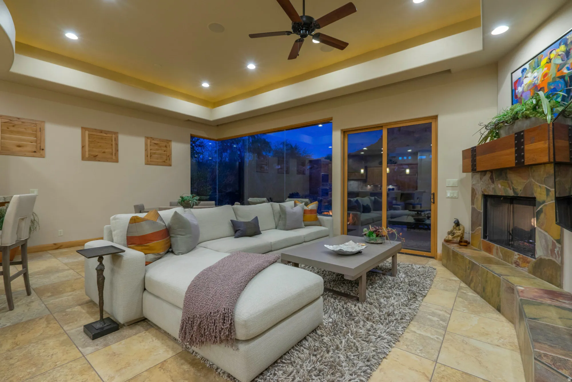 Living room with a raised ceiling, ceiling fan, recessed lighting, and a stone fireplace