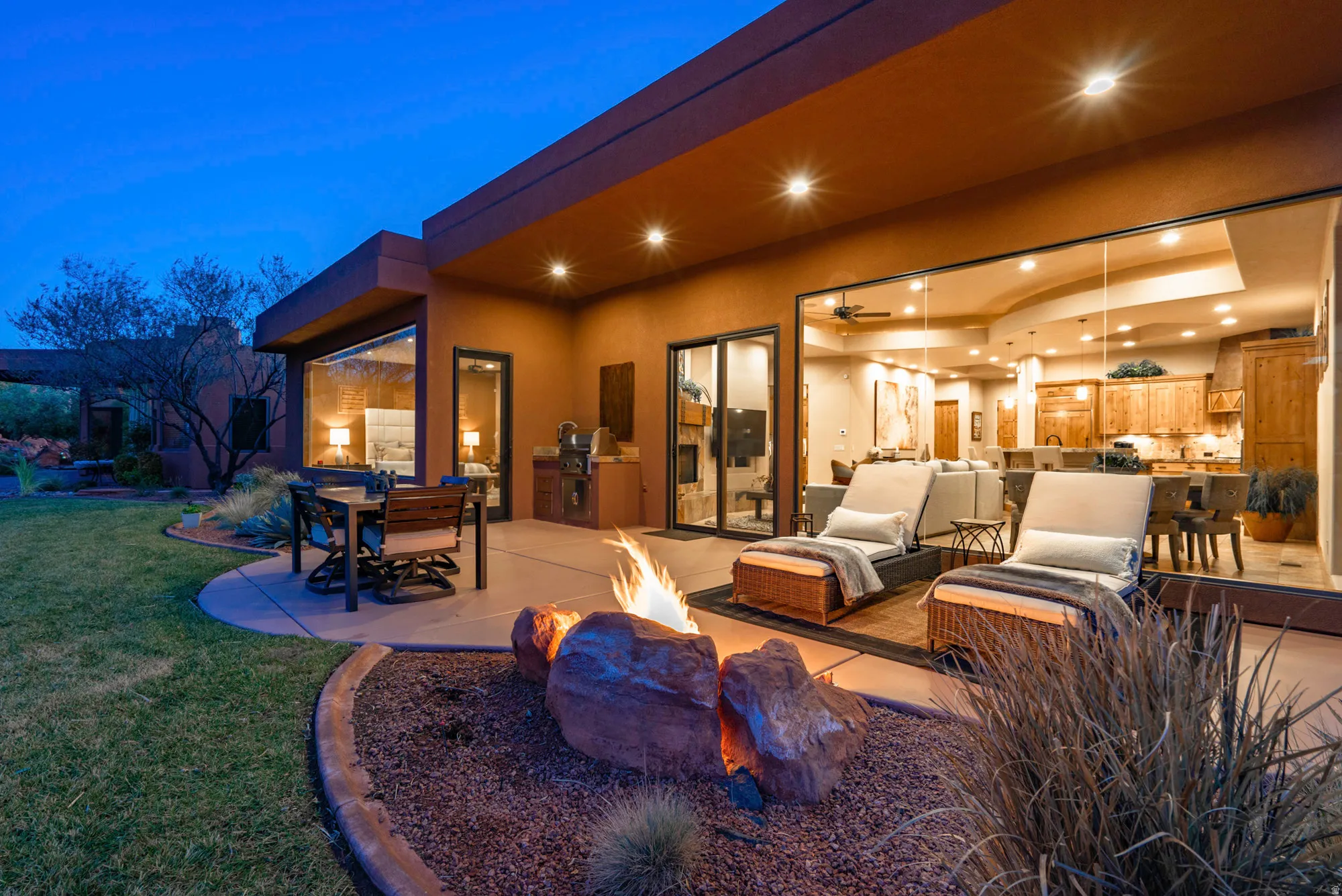 Patio terrace at dusk with an outdoor kitchen, an outdoor fire pit, an outdoor living / dining area, a patio area, and a lawn