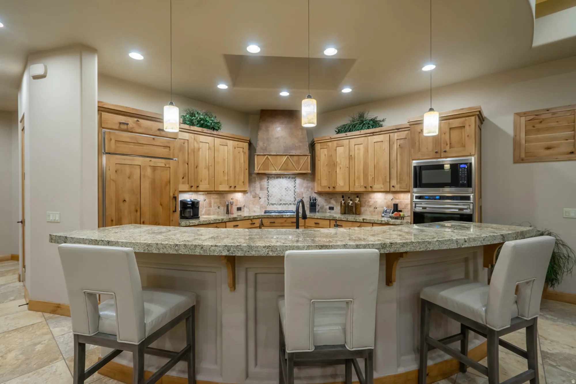 Kitchen with a breakfast bar area, light wood finish cabinetry, light stone countertops, decorative backsplash, and stainless steel appliances