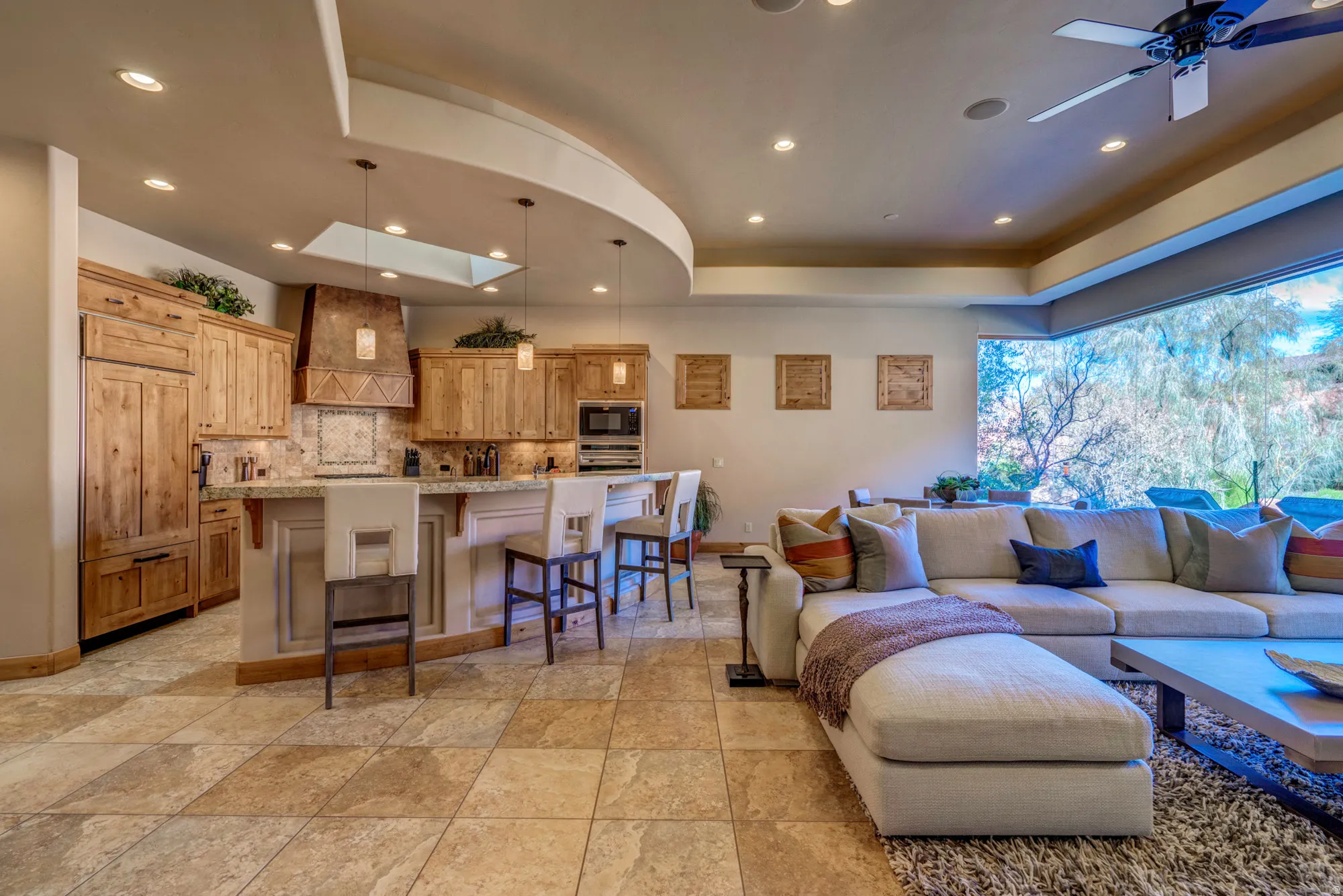 Living room with a skylight, ceiling fan, light stone finish flooring, and recessed lighting