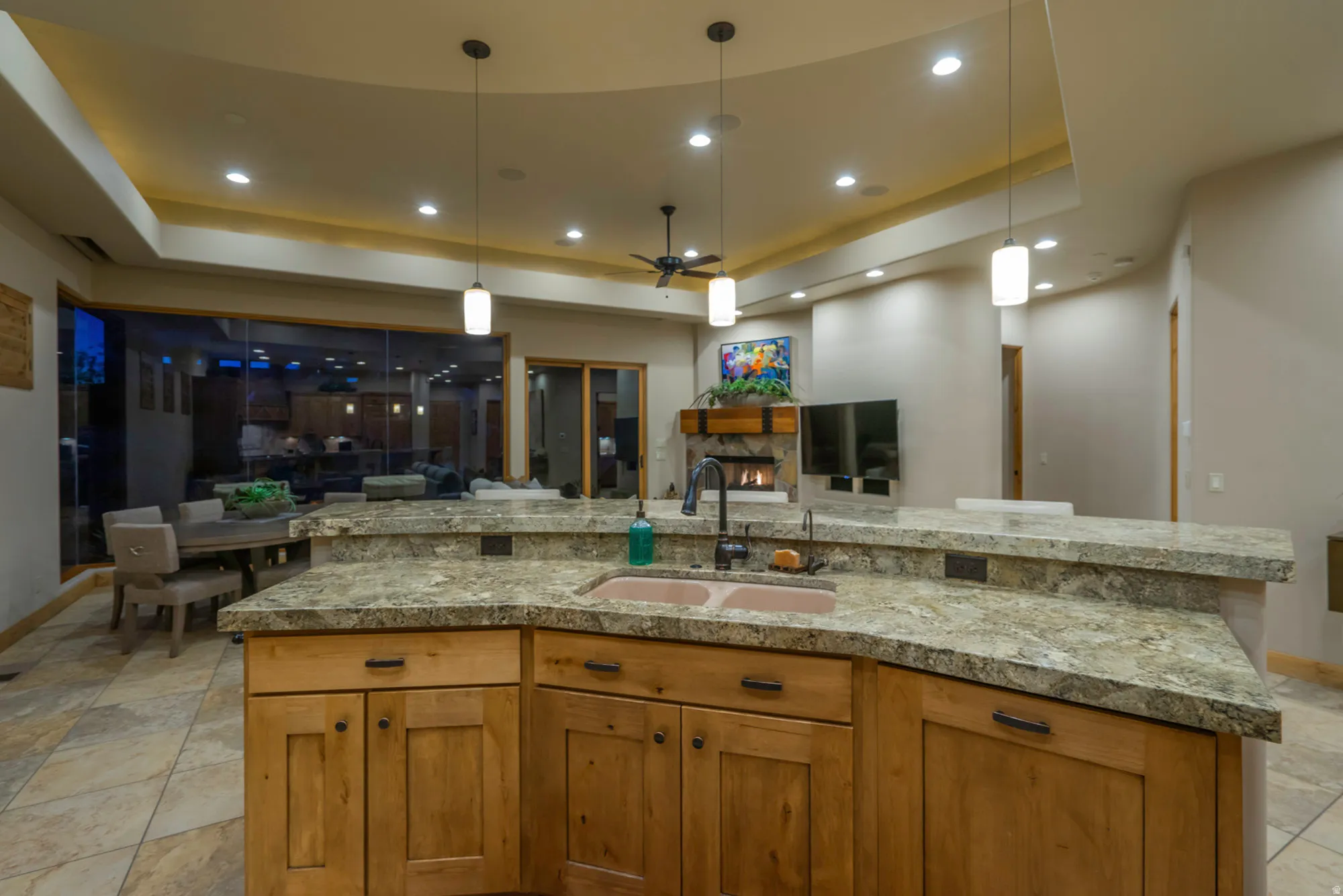 Kitchen with a raised ceiling, ceiling fan, open floor plan, wood finish cabinets, and decorative light fixtures