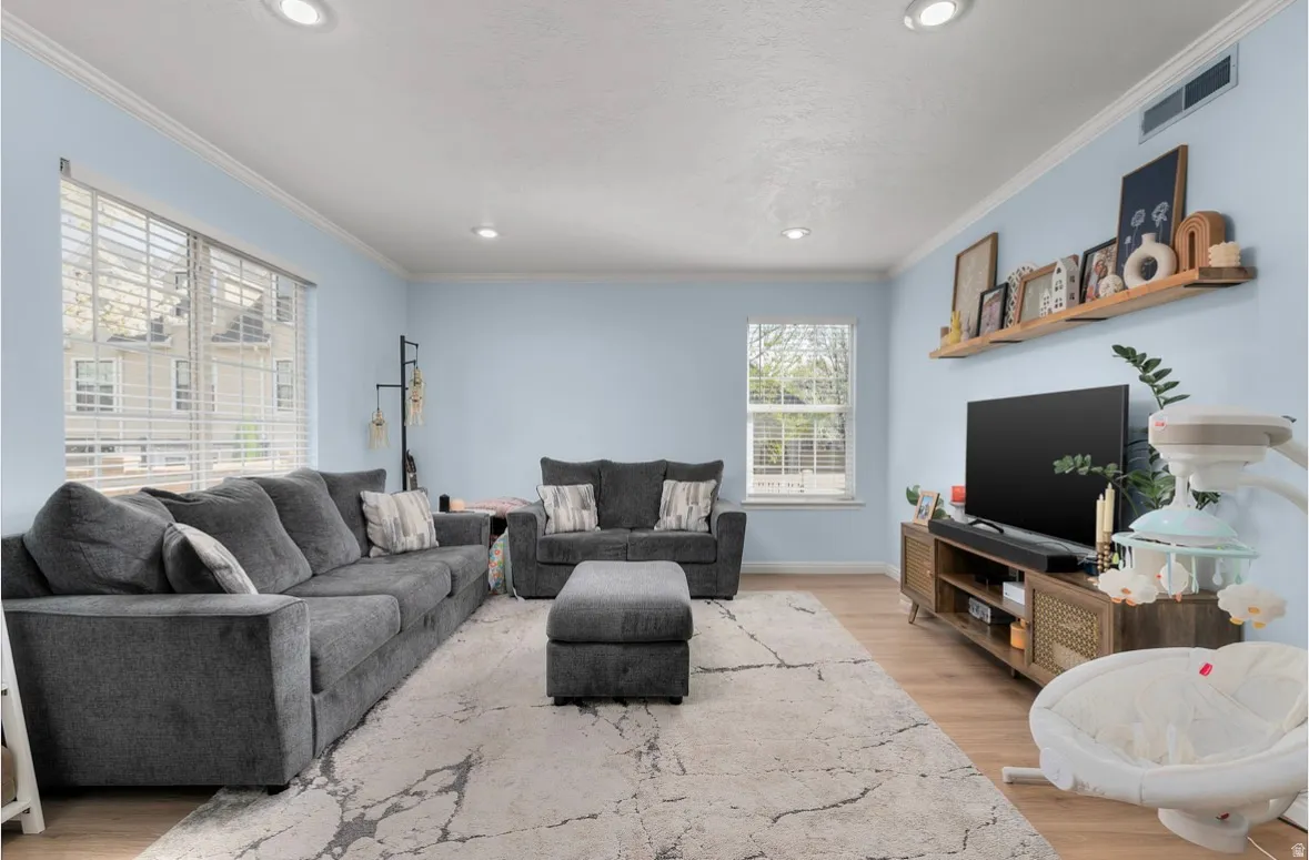 Living room with light wood-style floors, crown molding, and recessed lighting