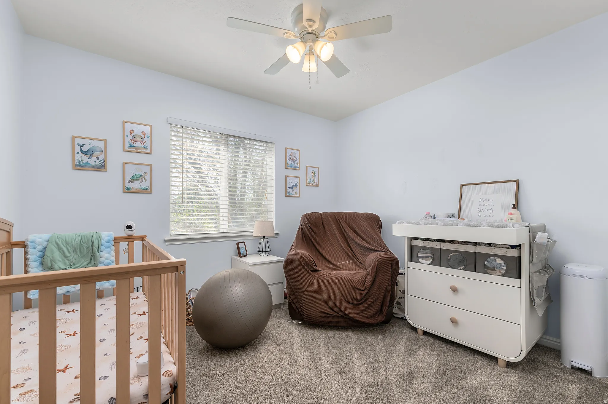 Carpeted bedroom featuring a crib and a ceiling fan