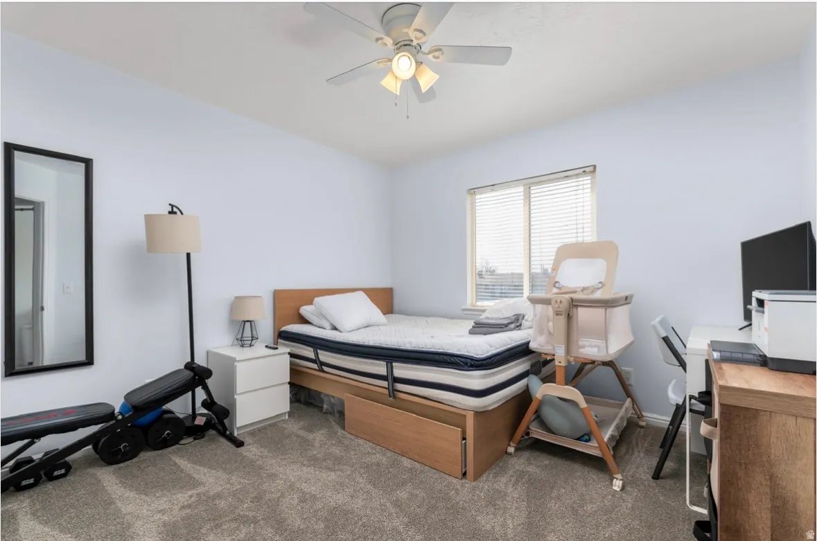 Bedroom with ceiling fan, dark colored carpet, and an office area
