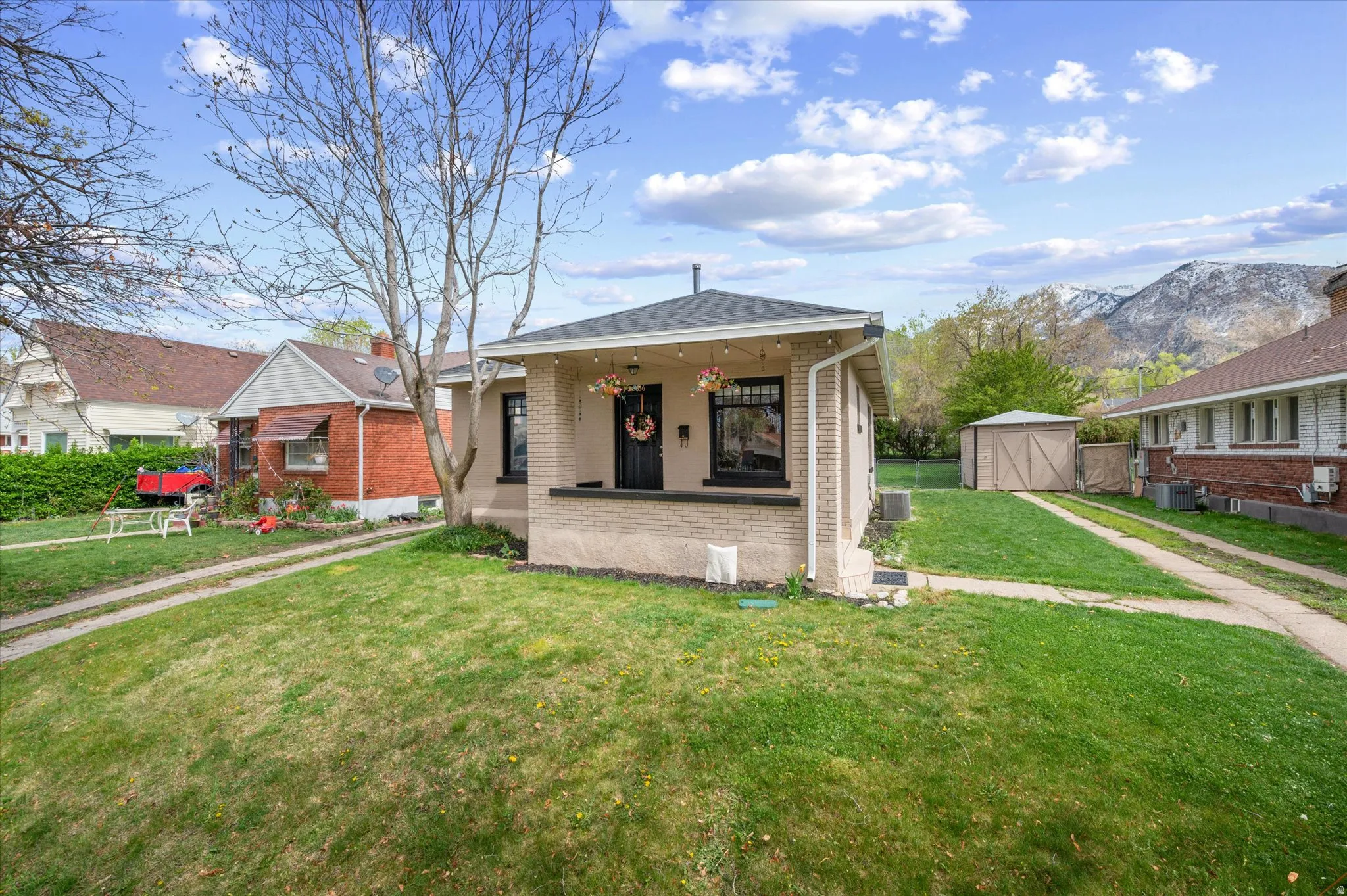 Bungalow-style house featuring brick siding, a front lawn, a mountain view, a storage shed, and a patio