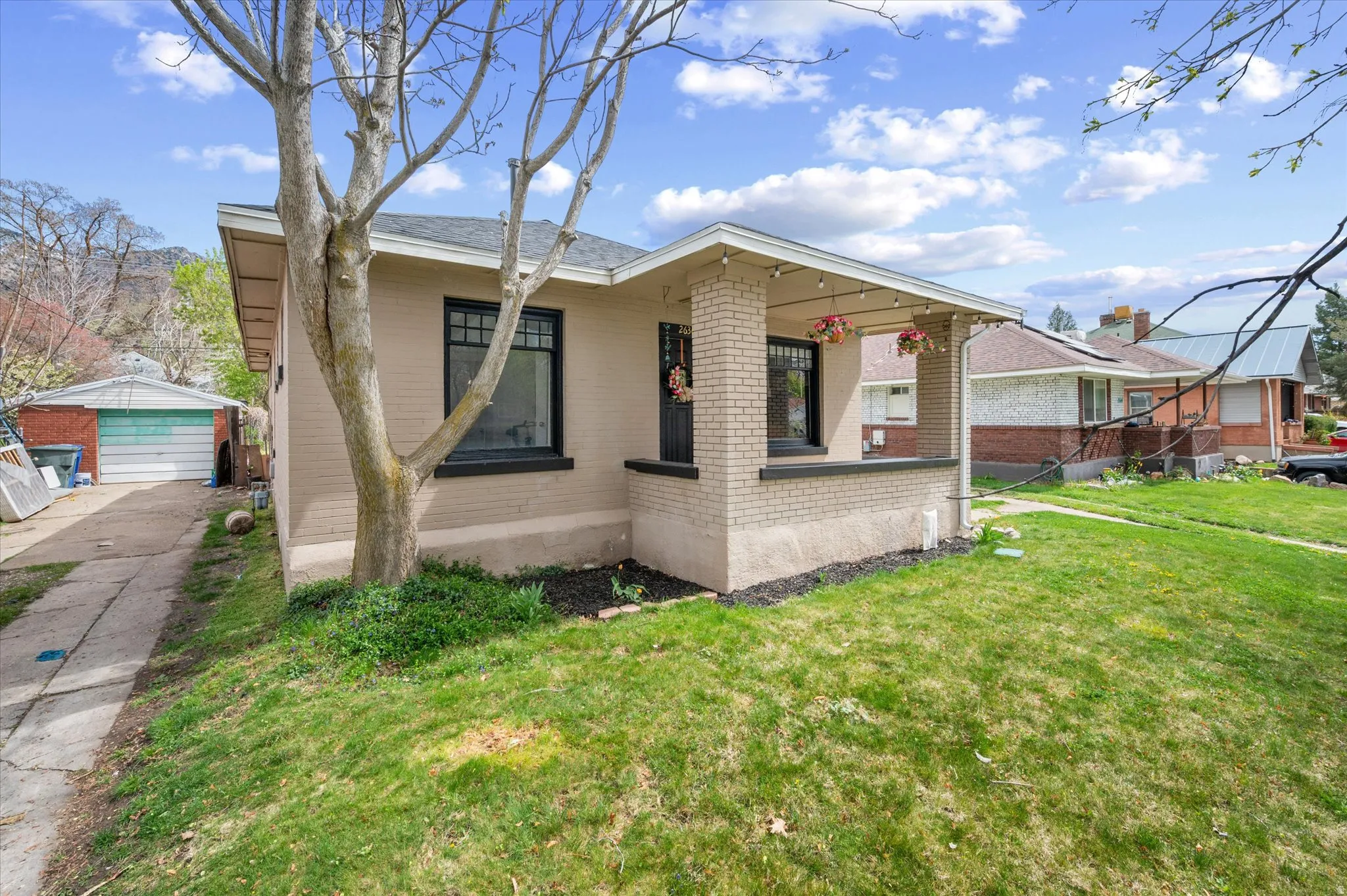 Bungalow-style house with brick siding, a front yard, an outbuilding, and a detached garage