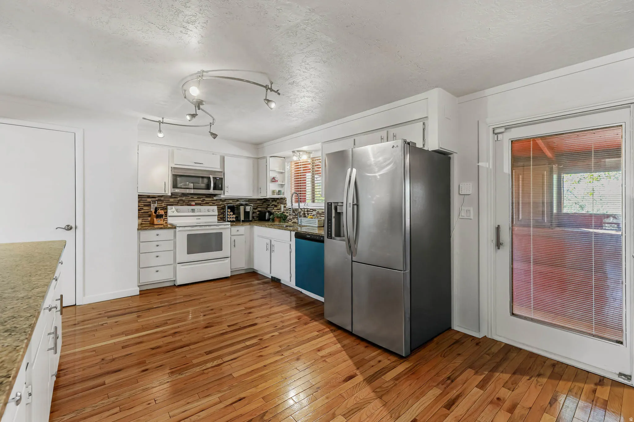 Kitchen with stainless steel appliances, white cabinetry, a textured ceiling, light wood-type flooring, and decorative backsplash