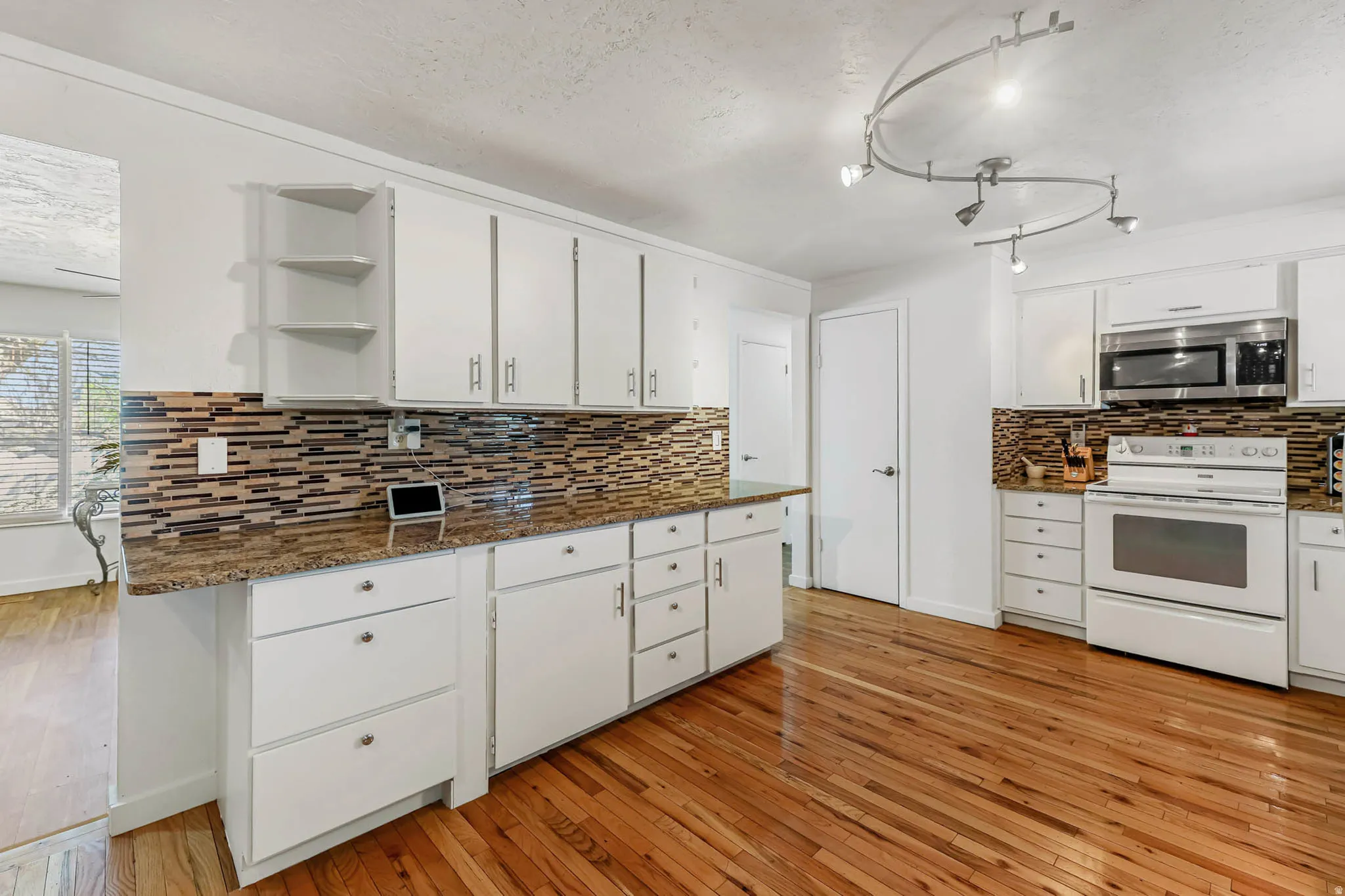 Kitchen with white range with electric stovetop, white cabinets, open shelves, light wood-style flooring, and a textured ceiling