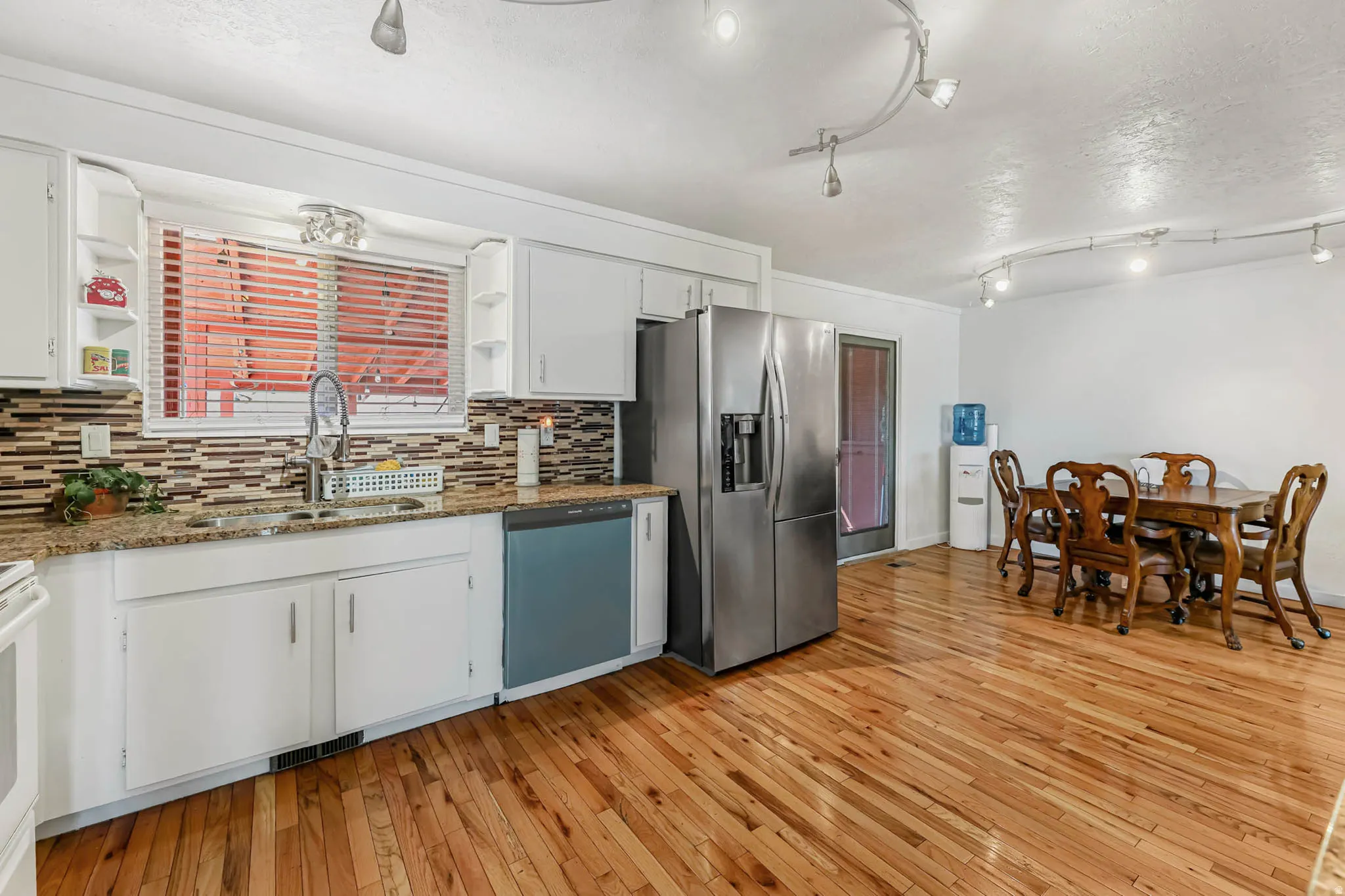 Kitchen with light wood finished floors, stainless steel refrigerator with ice dispenser, dishwasher, white cabinetry, and a textured ceiling