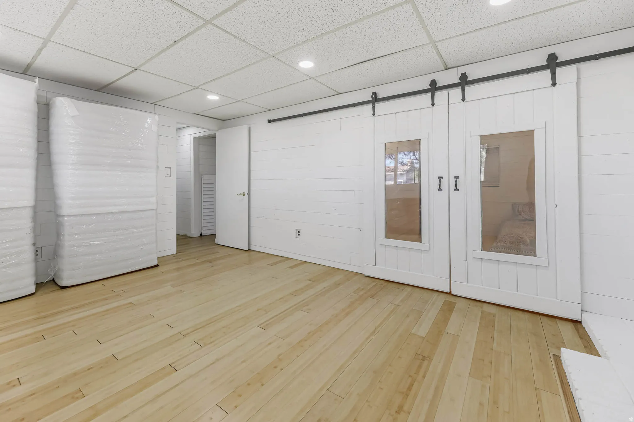 Unfurnished bedroom featuring a paneled ceiling, recessed lighting, light wood-style floors, wood walls, and a barn door