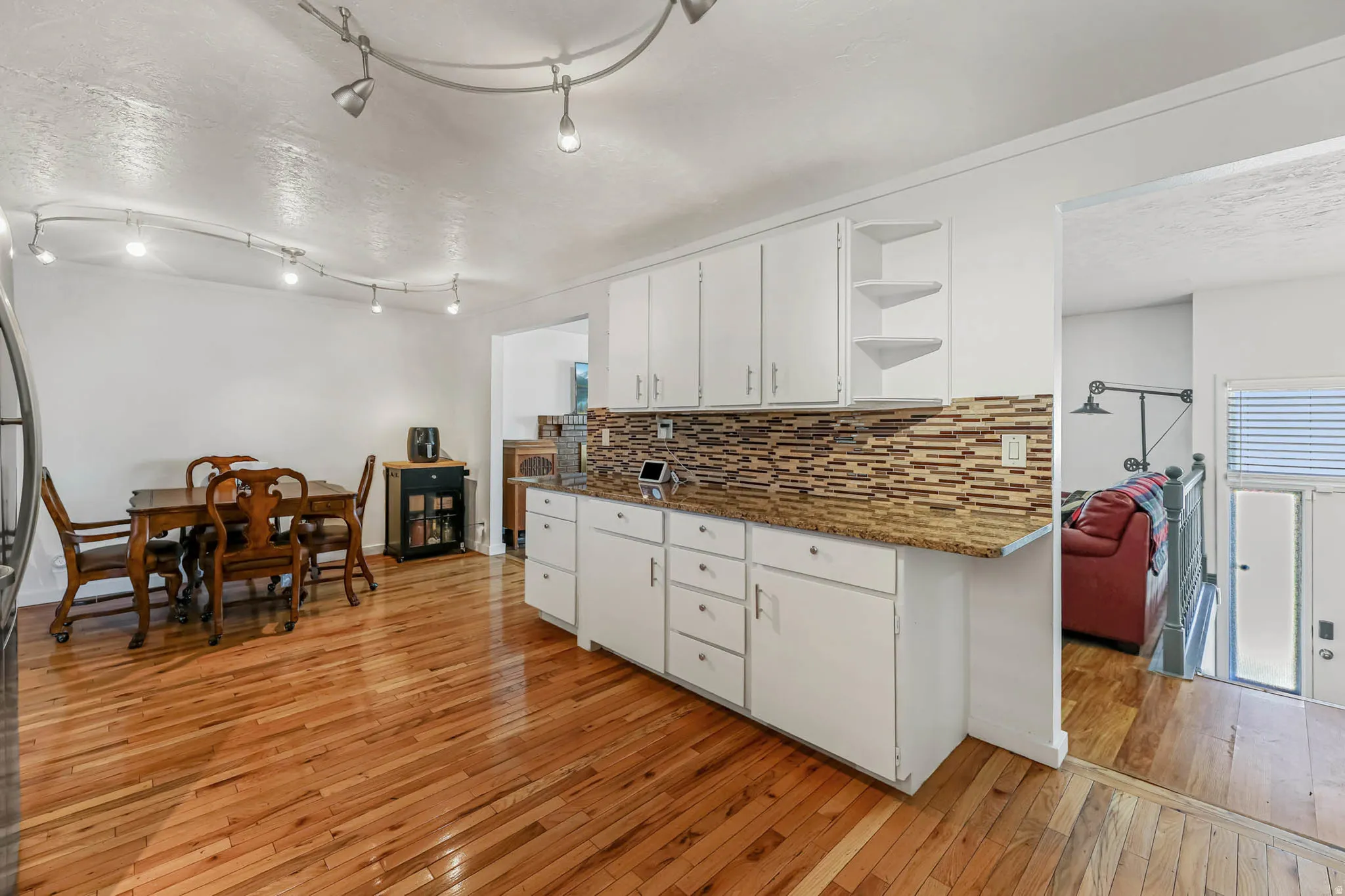 Kitchen with a textured ceiling, light wood-style flooring, white cabinets, open shelves, and tasteful backsplash