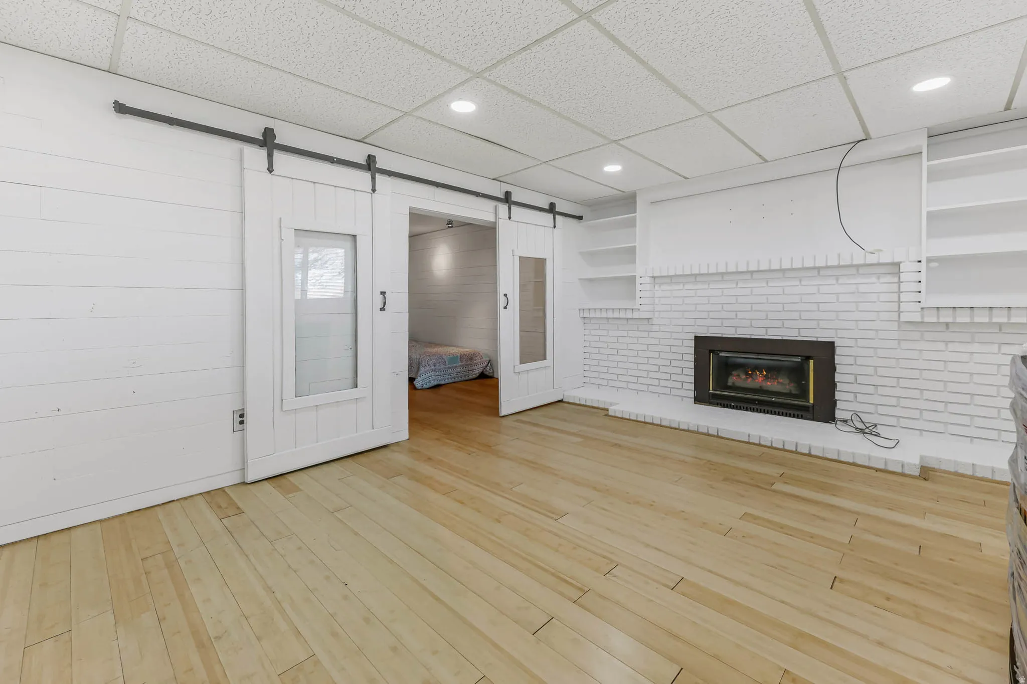 Unfurnished living room featuring a drop ceiling, a barn door, recessed lighting, a fireplace, and light wood finished floors