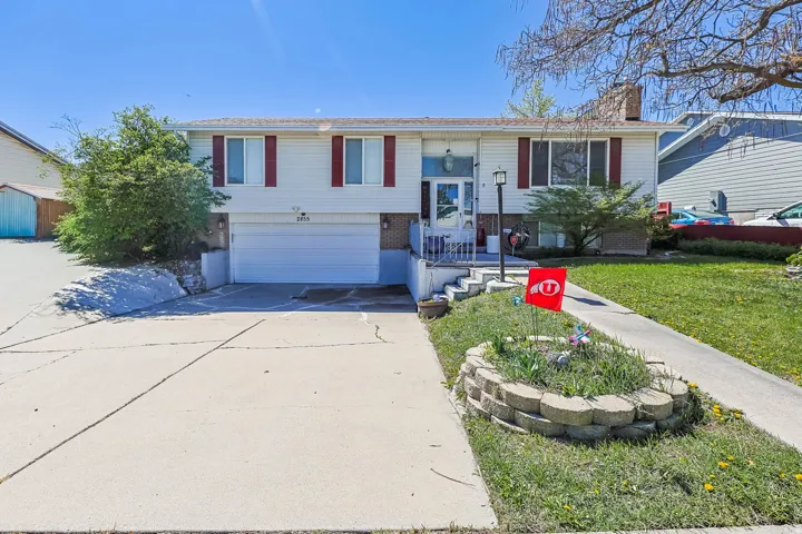 Split foyer home with brick siding, an attached garage, concrete driveway, a chimney, and a front yard