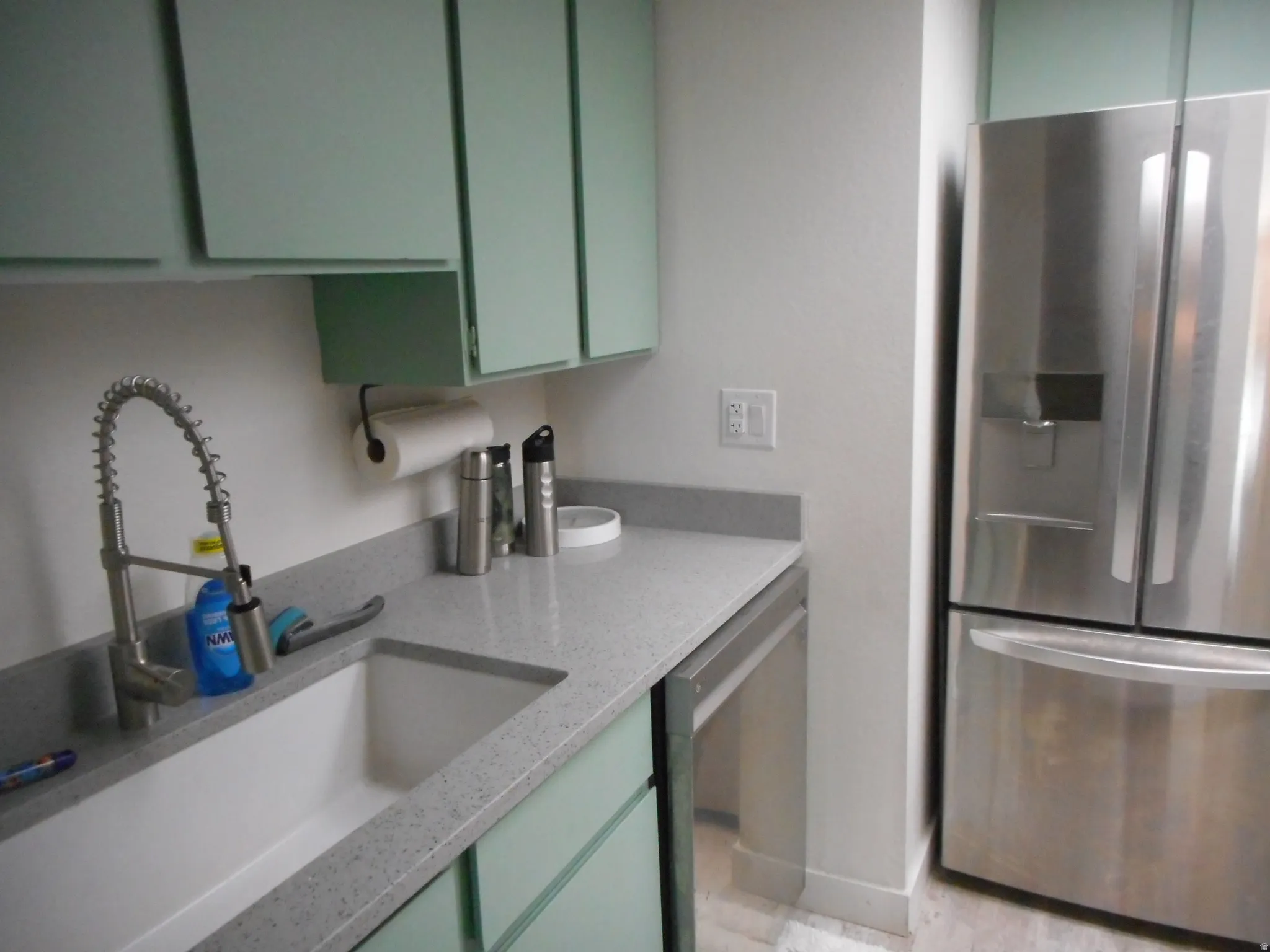 Kitchen with stainless steel appliances, green cabinetry, and light stone countertops