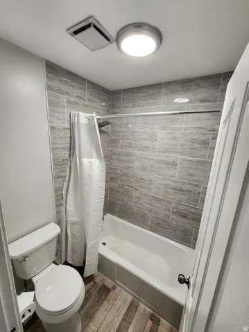 Full bath with shower / bath combination with curtain and wood tiled floors
