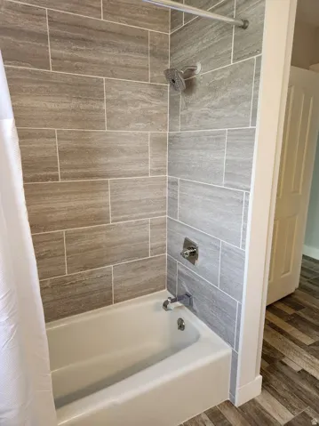 Bathroom with shower / bath combination with curtain and dark wood-style flooring