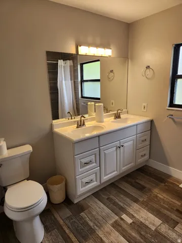 Bathroom featuring double vanity, dark wood-style flooring, and curtained shower