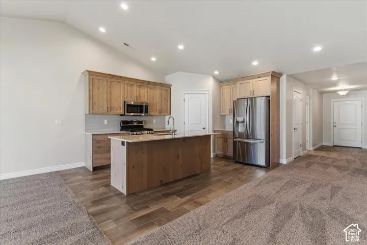 Kitchen with stainless steel appliances, decorative backsplash, wood finish floors, an island with sink, and recessed lighting