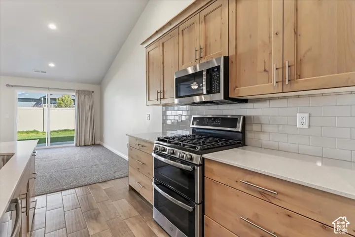Kitchen featuring stainless steel appliances, lofted ceiling, light stone counters, backsplash, and wood finish floors